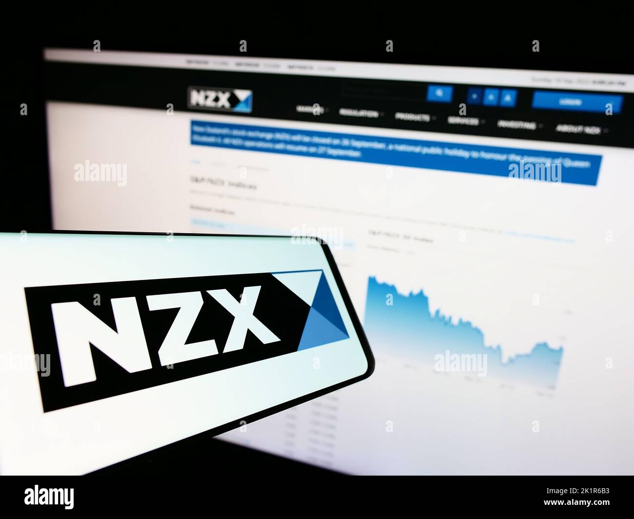 Mobile phone with logo of financial company New Zealand's Exchange (NZX) on screen in front of website. Focus on center-right of phone display. Stock Photo