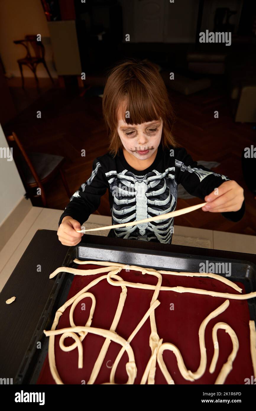 Boy child in costume and skeleton make-up preparing pastries for baking on a baking sheet for the holiday halloween at home Stock Photo