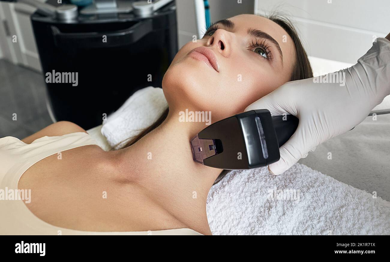 Pretty woman getting rf-lifting for her neck and body. Rf lifting procedure at beauty parlour with beautician Stock Photo