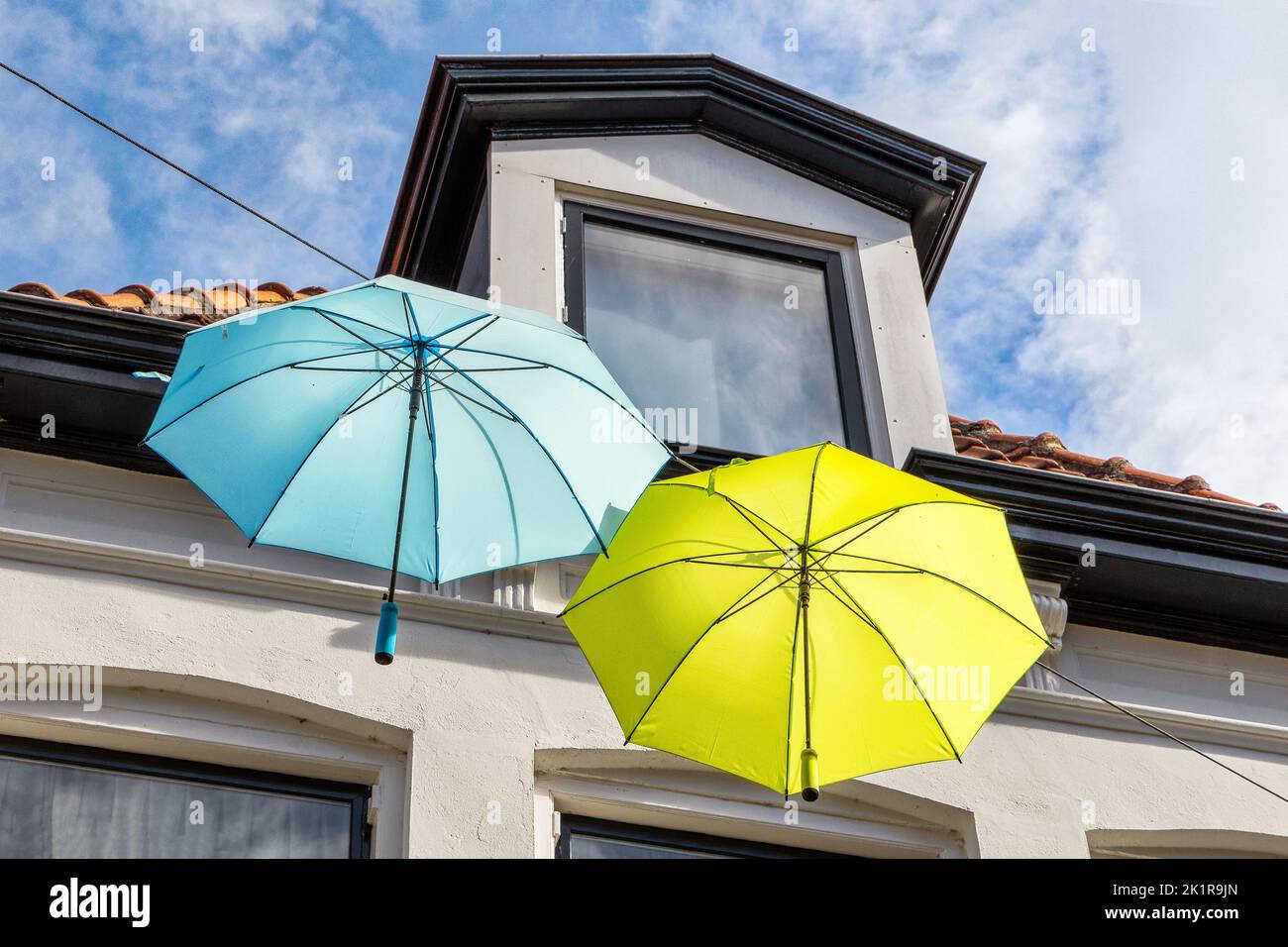 Colorful umbrellas in the air against blue sky with clouds Stock Photo