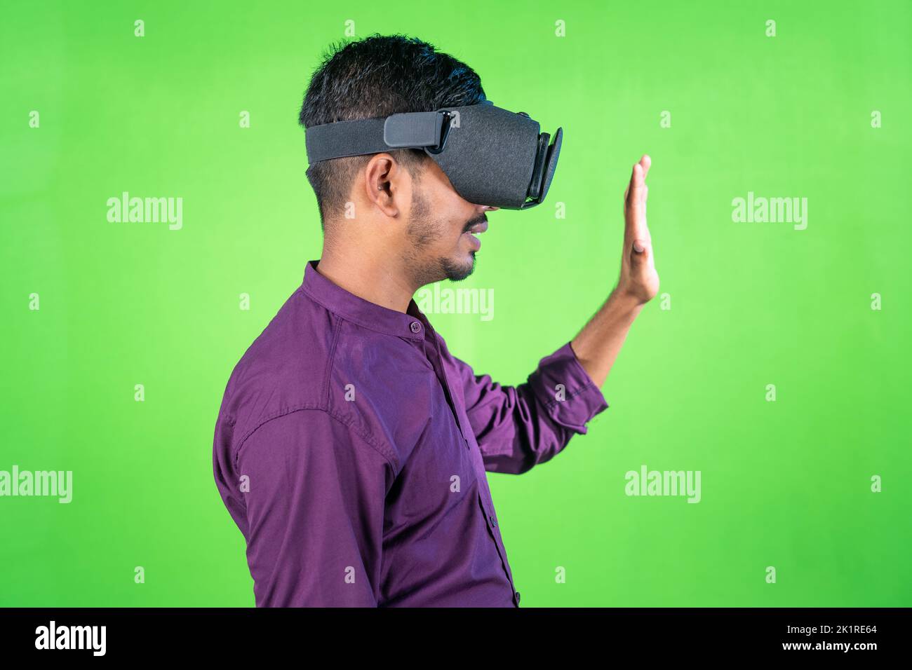 side view of young man with VR or virtual reality headset saying greeting by saying hi in metaverse on green screen background - concept of technology Stock Photo