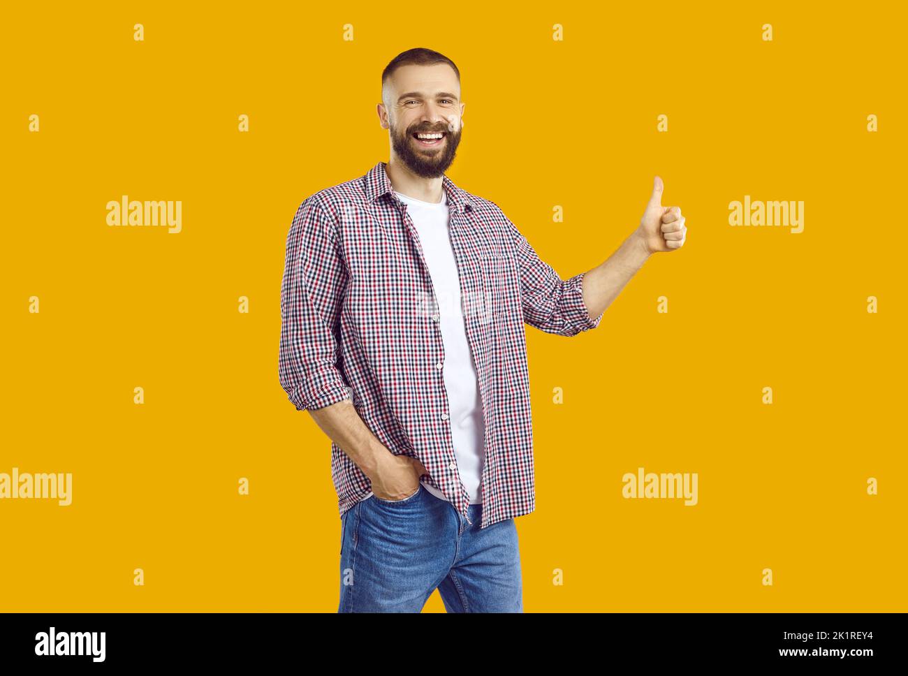 Cheerful young man isolated on orange yellow background smiling and giving thumbs up Stock Photo