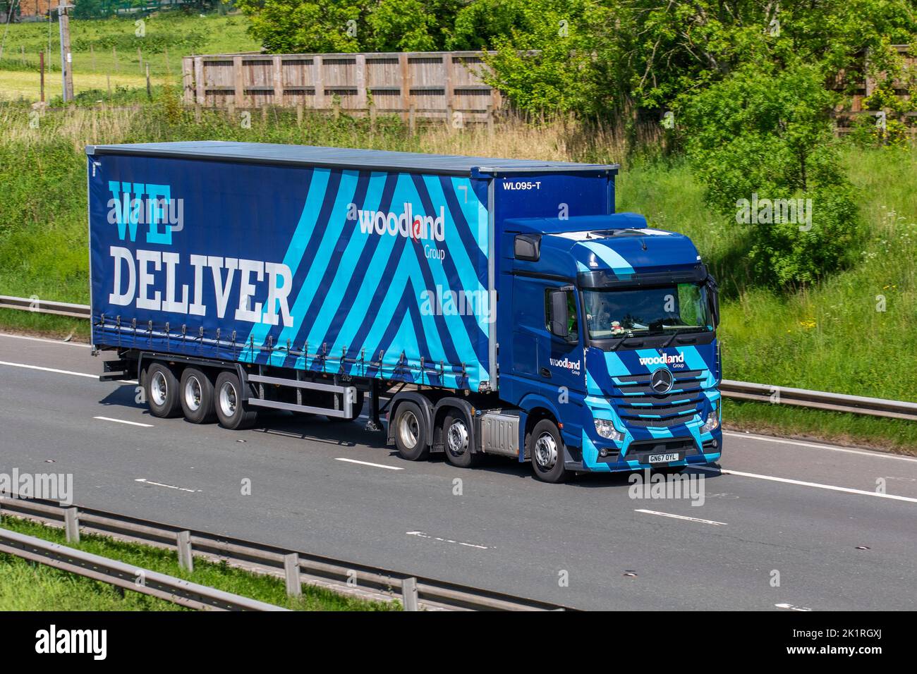 Woodland Group Haulage 'WE DELIVER' trucks, lorry, heavy-duty vehicles, transportation, truck, cargo carrier, blue Mercedes Benz vehicle, European commercial transport industry HGV, M6 at Manchester, UK Stock Photo