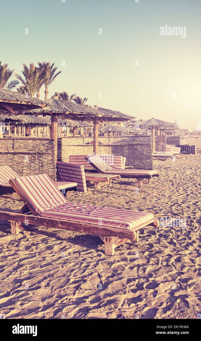 Retro stylized picture of sunbeds and umbrellas on beach, summer vacation concept. Stock Photo