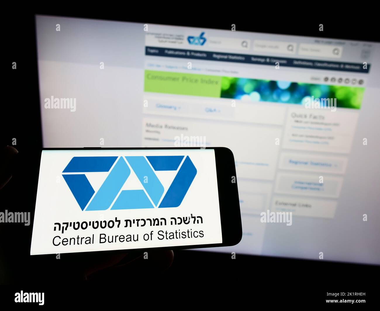 Person holding smartphone with logo of Israel Central Bureau of Statistics (CBS) on screen in front of website. Focus on phone display. Stock Photo