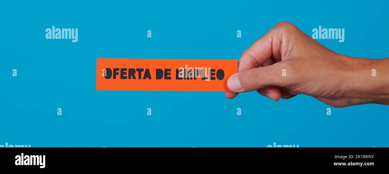 a man is holding an orange paper sign with the text job offer written in spanish, on a blue background, in a panoramic format to use as web banner or Stock Photo