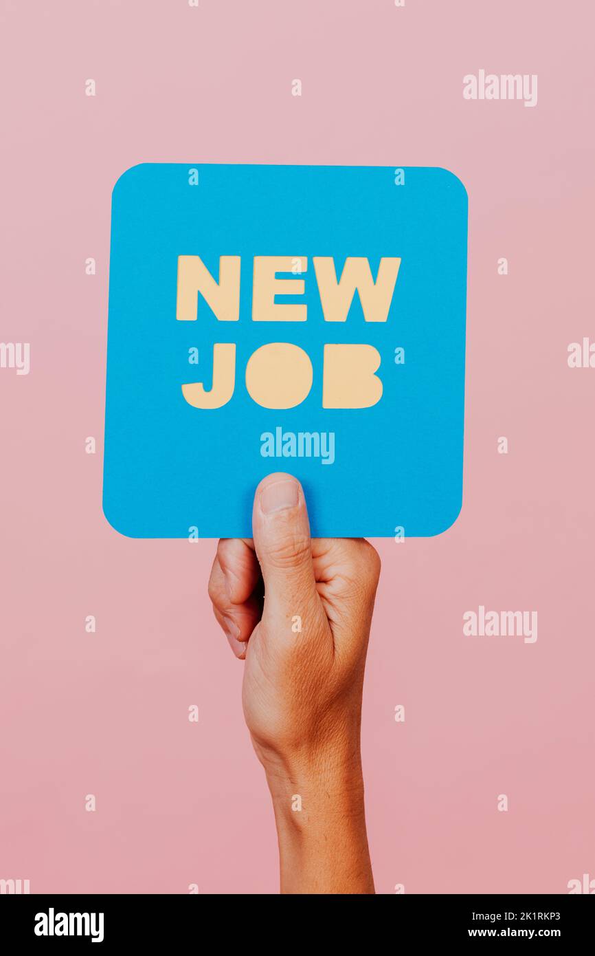 closeup of a man holding a blue paper signboard in the shape of a speech bubble that reads the text new job, on a pink background Stock Photo