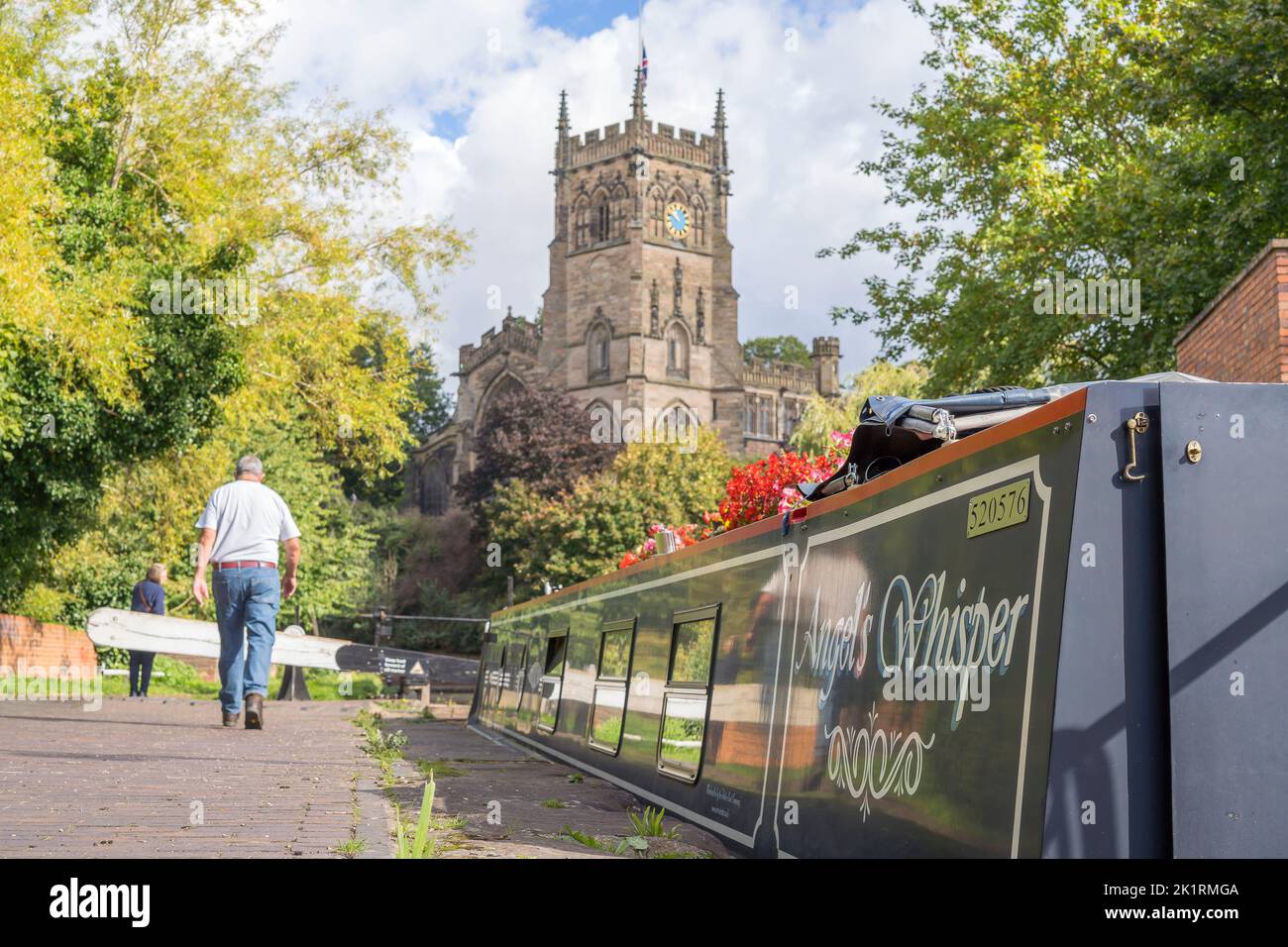 Rear view of a man walking alongside his boat heading to the front of his boat and the lock gate exit. A church with cloudy skies is the backdrop to t Stock Photo
