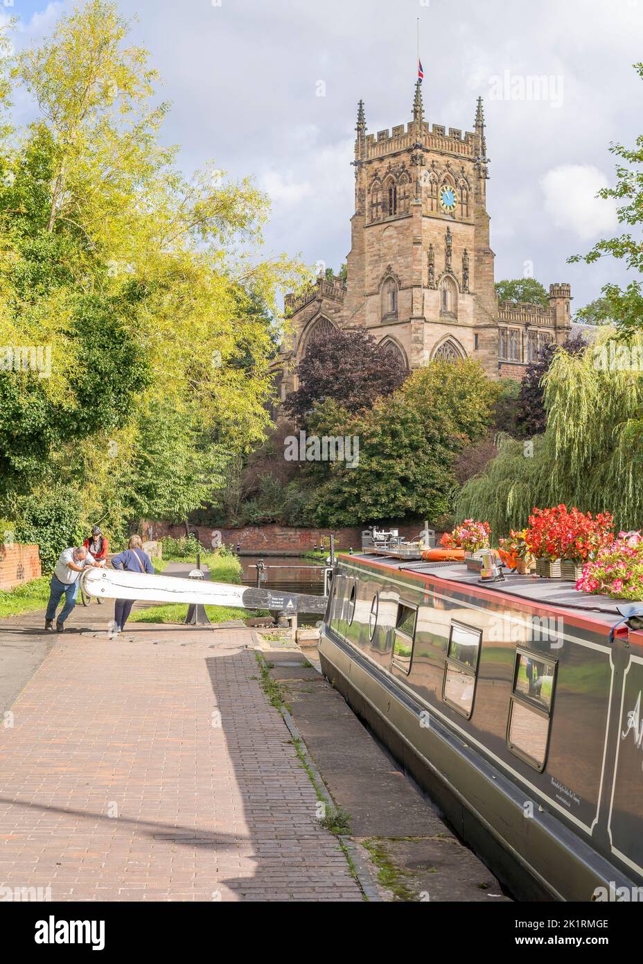 Retired couple opening Kidderminster canal lock gate (by St Mary's church) for their holiday narrowboat to pass through beautiful Worcestershire, UK. Stock Photo