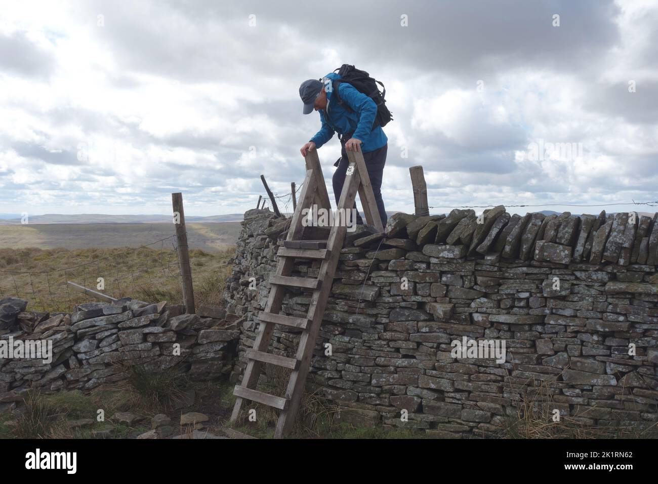 Lone Man Climbing Wooden Ladder Stile over Stone Wall near the Summit of 'Buckden Pike' in Wharfedale, Yorkshire Dales National Park, England, UK. Stock Photo
