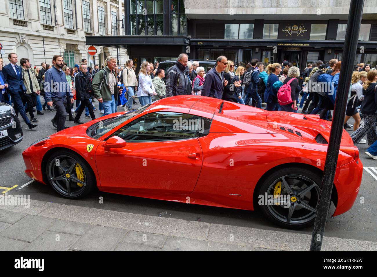 Crowds of people heading to Hyde Park for Queen Elizabeth II funeral screening pass a red Ferrari on Curzon Street, 19th September 2022, London, UK Stock Photo