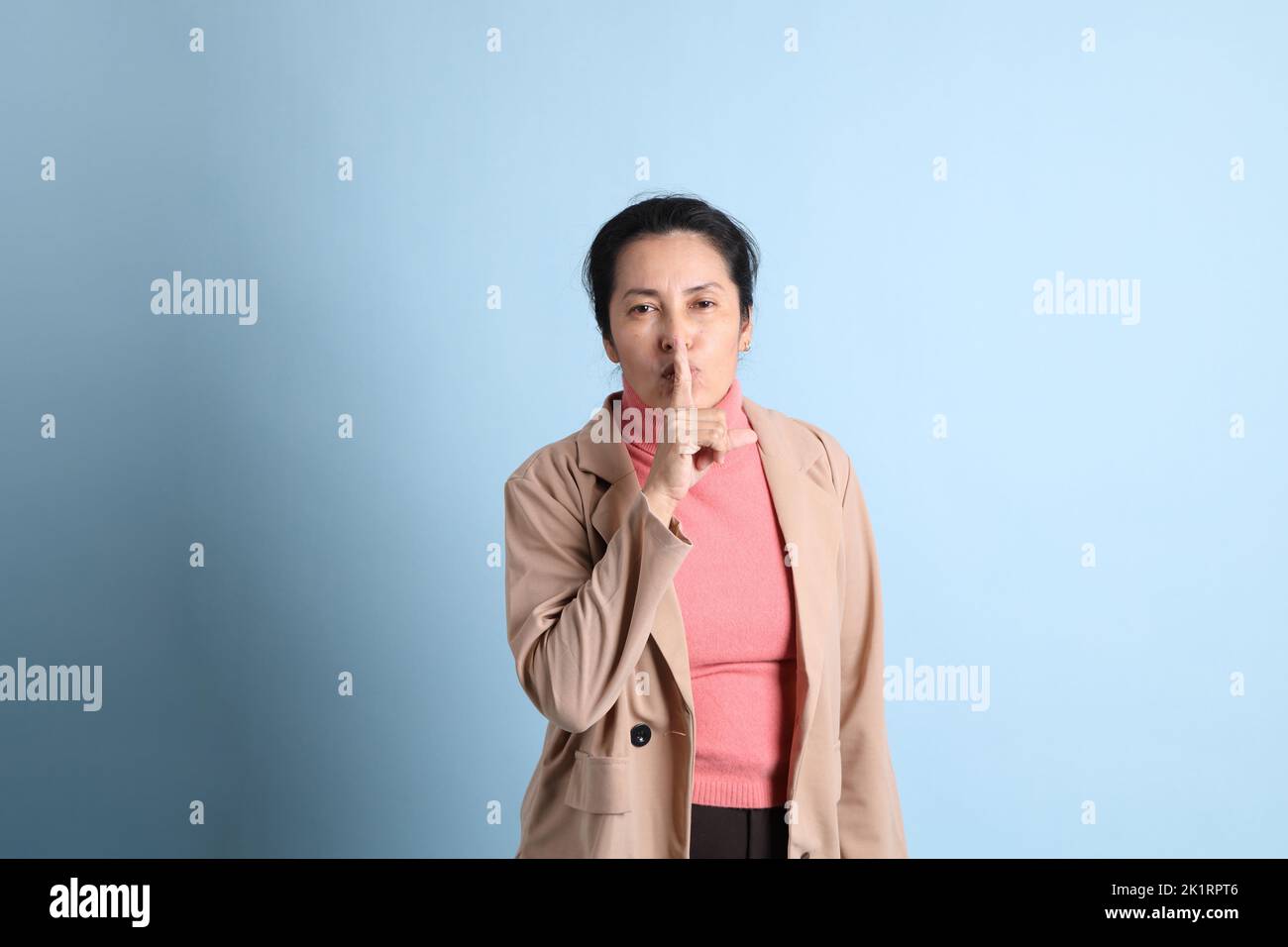 The senior Asian woman with pink shirt brown blazer on the blue background. Stock Photo