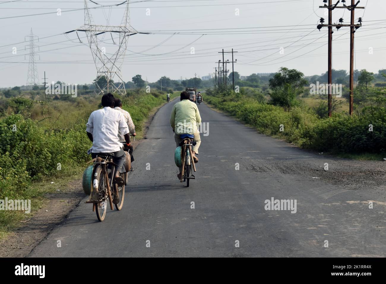A beautiful photo of an Indian old and young man farmer riding his bicycle (bike or cycle) in a nearby village along the fields or farmlands or farms Stock Photo