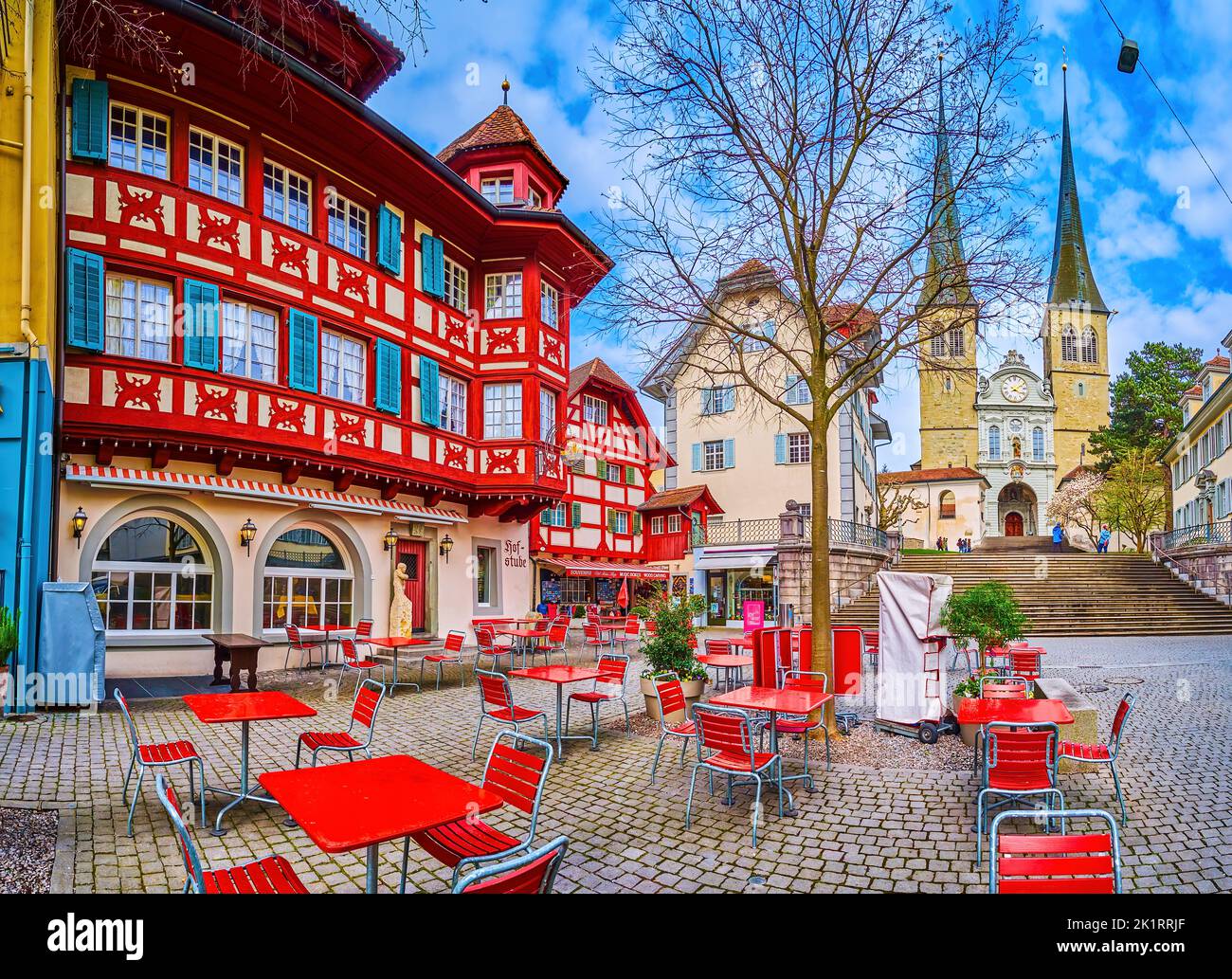 LUCERNE, SWITZERLAND - MARCH 30, 2022: Panorama of the small pedestrian street with outdoor cafe and St. Leodegar im Hof church on background, on Marc Stock Photo