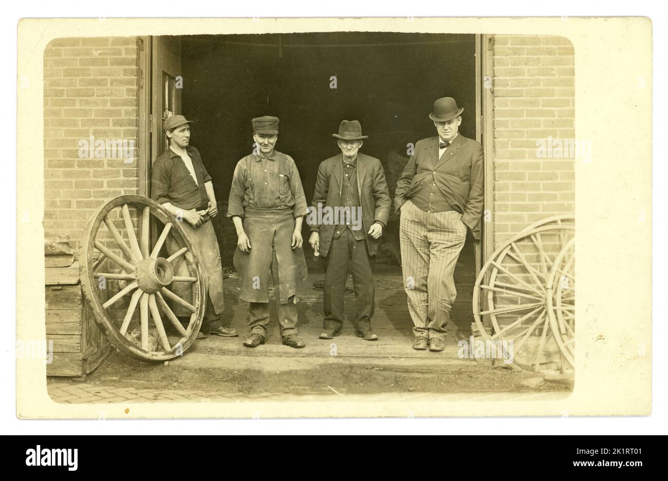 Original very clear, early 1900's American postcard of 3 wheelwrights, overseer maybe in pinstripe trousers, bowler hat, with cart wheels posing for a photo portrait outside their workshop. Some amazing real characters, workwear fashions, bowler hats. Room for copy space.  U.S.A. Circa 1919 Stock Photo
