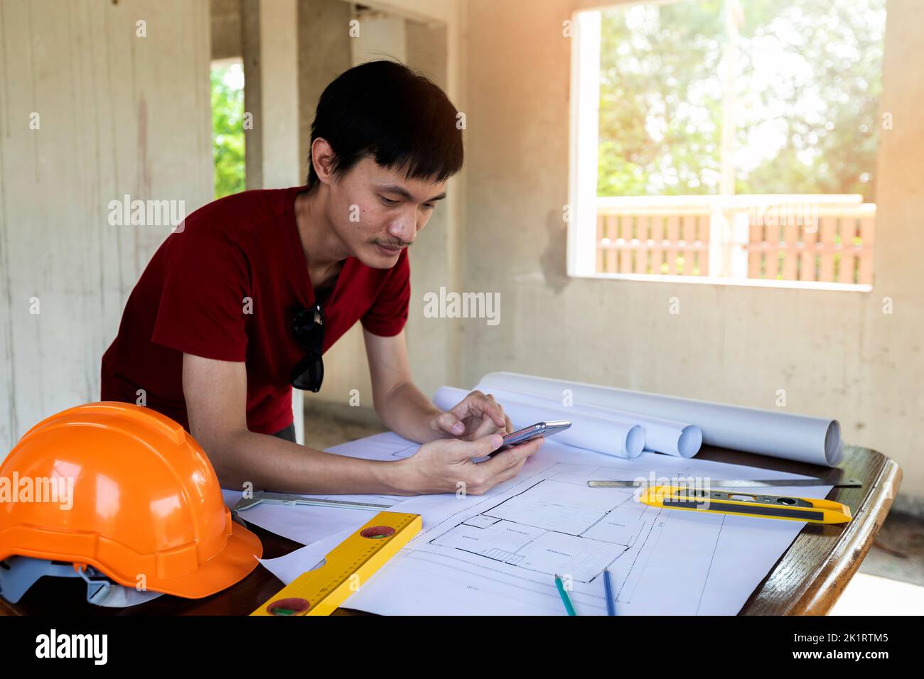 Engineer or Architect using cell phone on blueprint in building construction site. Stock Photo