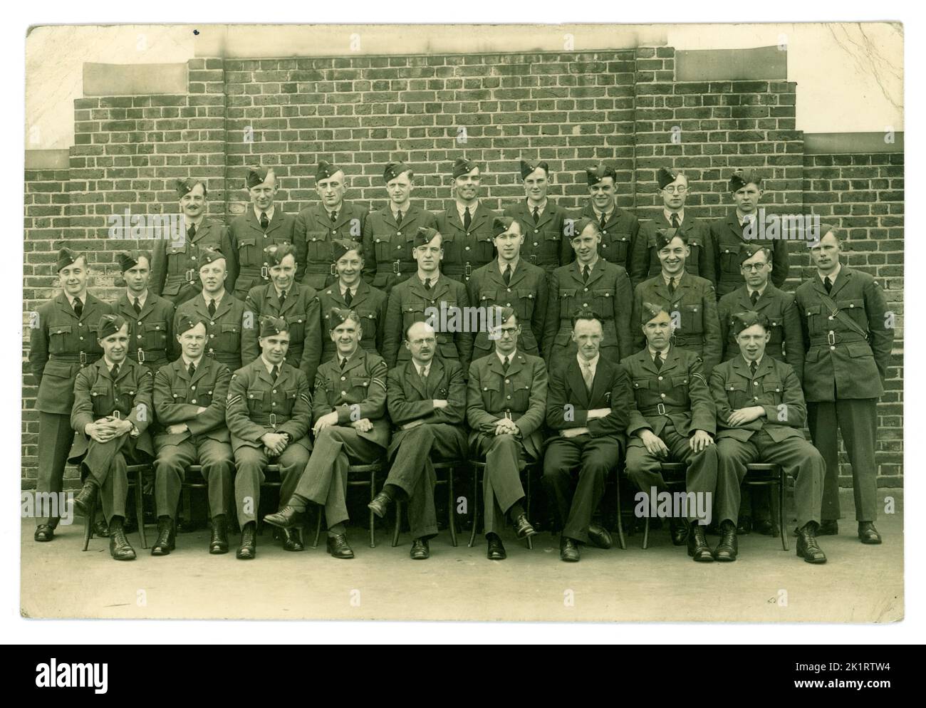 Original WW2 era Royal Air Force personnel (RAF) airmen wearing uniform of tunic and side caps. At air training school. There are examiners or non military personnel, pens in pockets sitting with them. Circa 1943, unknown location, U.K. Stock Photo