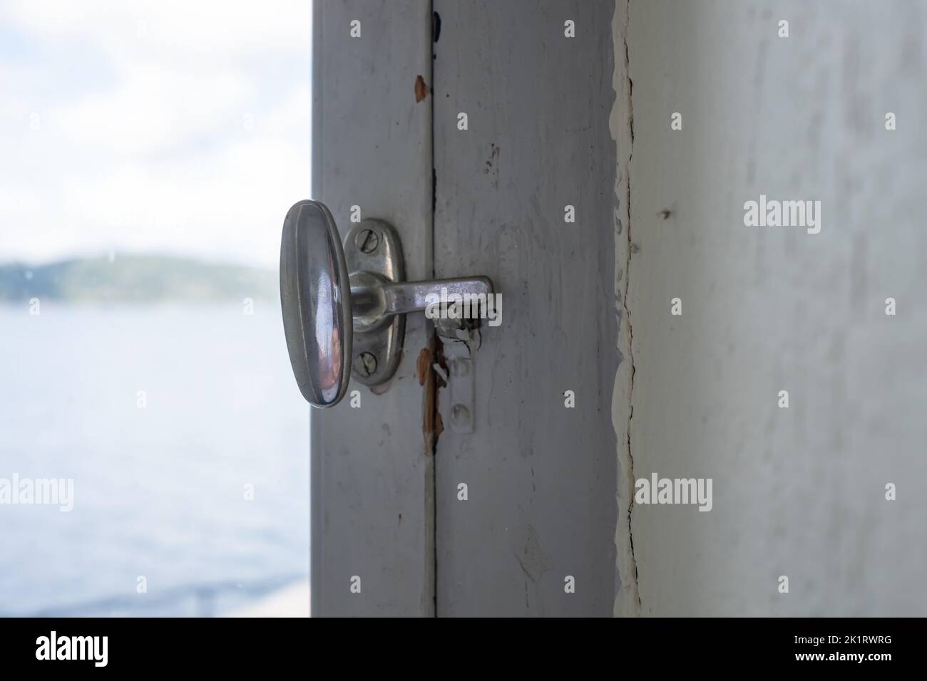Metal latch on the frame of an old white painted wooden window. Close-up. Stock Photo