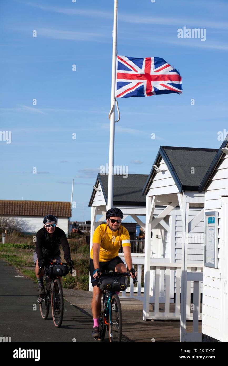 Two smiling,  male cyclists, pass under a union Jack flying at half mast,  during the period of national mourning, for Queen Elizabeth 2nd. Stock Photo