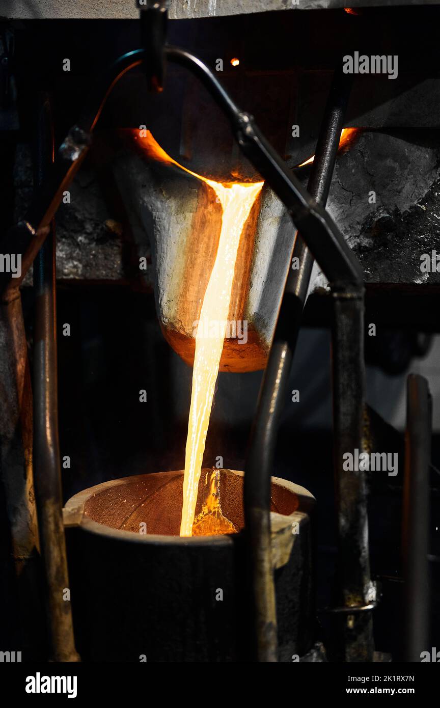 Melted liquid metal flow poured down from pot in furnace Stock Photo