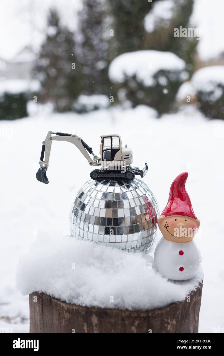 model of a toy metal excavator stands on a mirror disco ball, a souvenir snowman on a snow-covered stump. concept of christmas business greetings, win Stock Photo