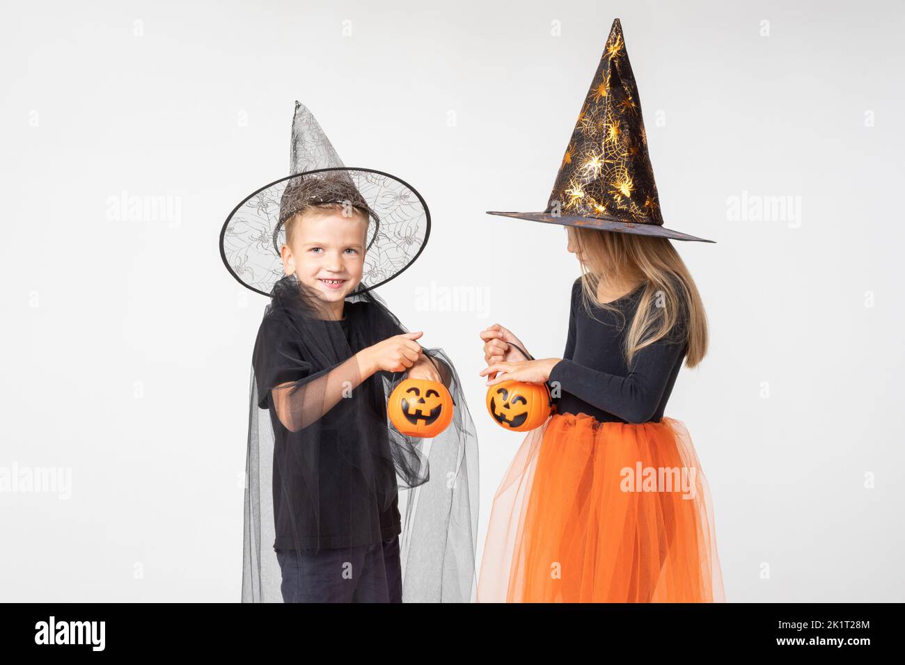 Kids Halloween. A beautiful girl in a witch costume and a boy in a wizard costume take out candy from a basket in the shape of Jack's lantern. Child h Stock Photo