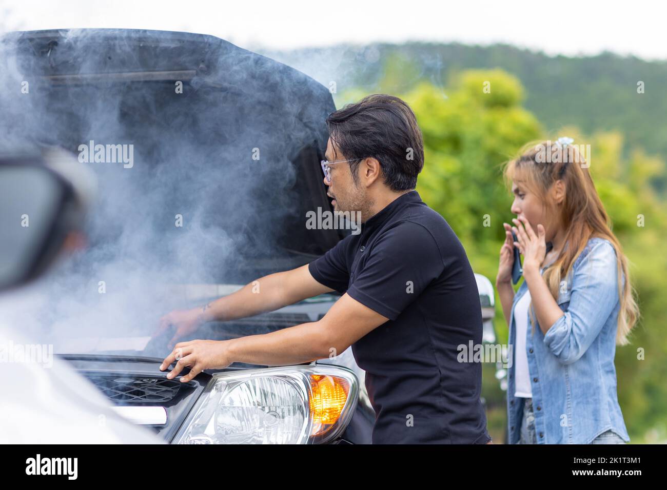 Car engine overheating, smoke out from engine front hood man help to check with shocked woman driver Stock Photo