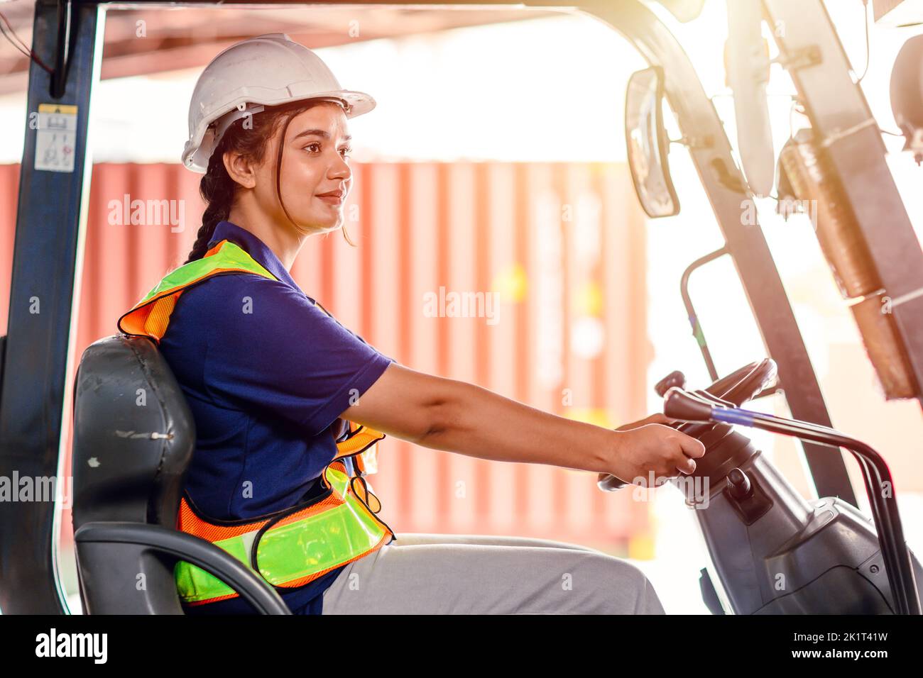 female forklift operator working in a warehouse. Portrait of young Indian woman driver sitting in forklift and smiling working in large warehouse Stock Photo