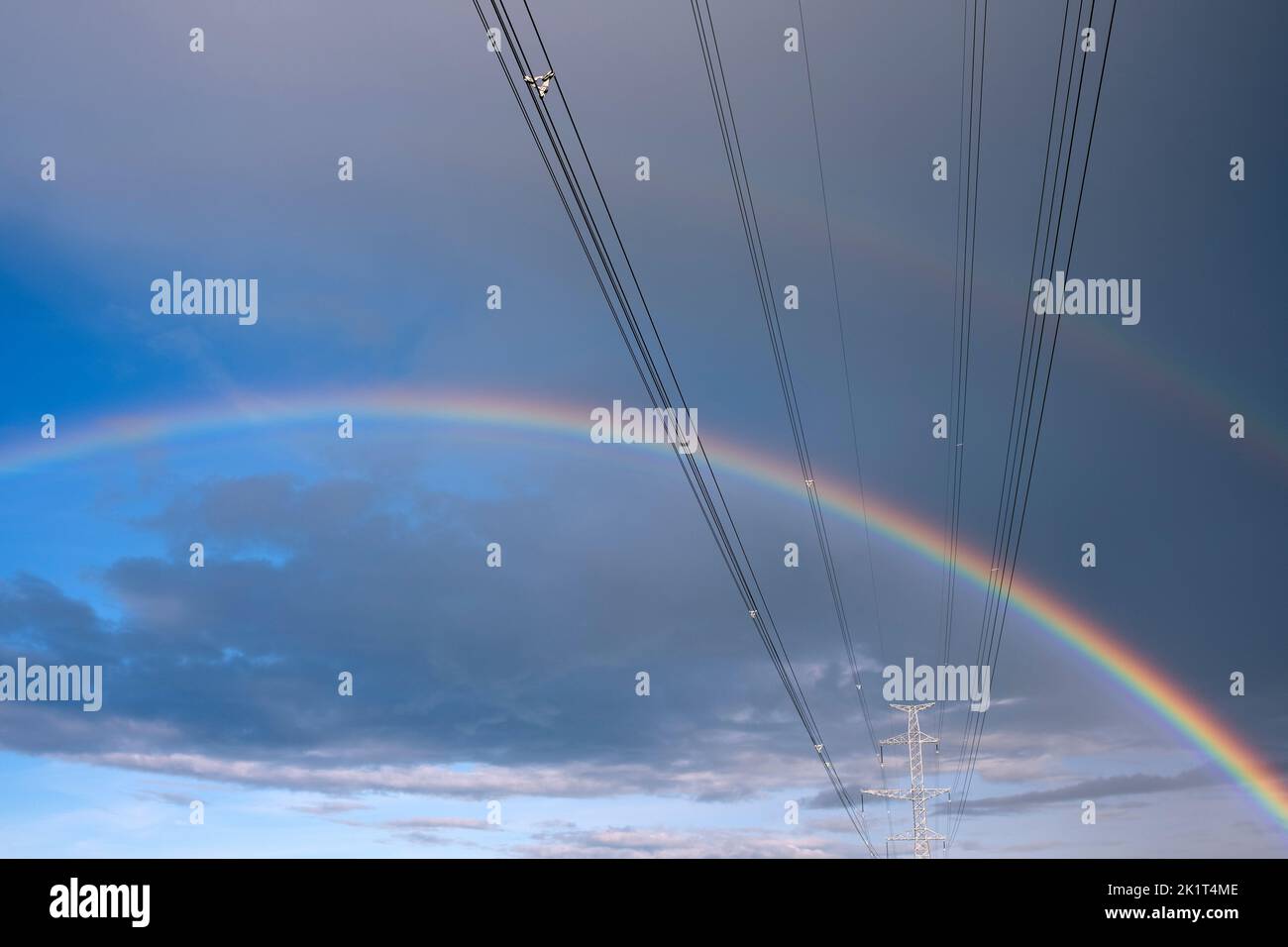 High-voltage power lines and double rainbow in the sky Stock Photo