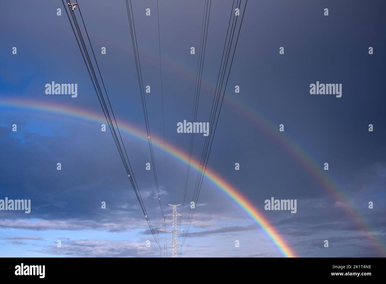 High-voltage power lines and double rainbow in the sky Stock Photo