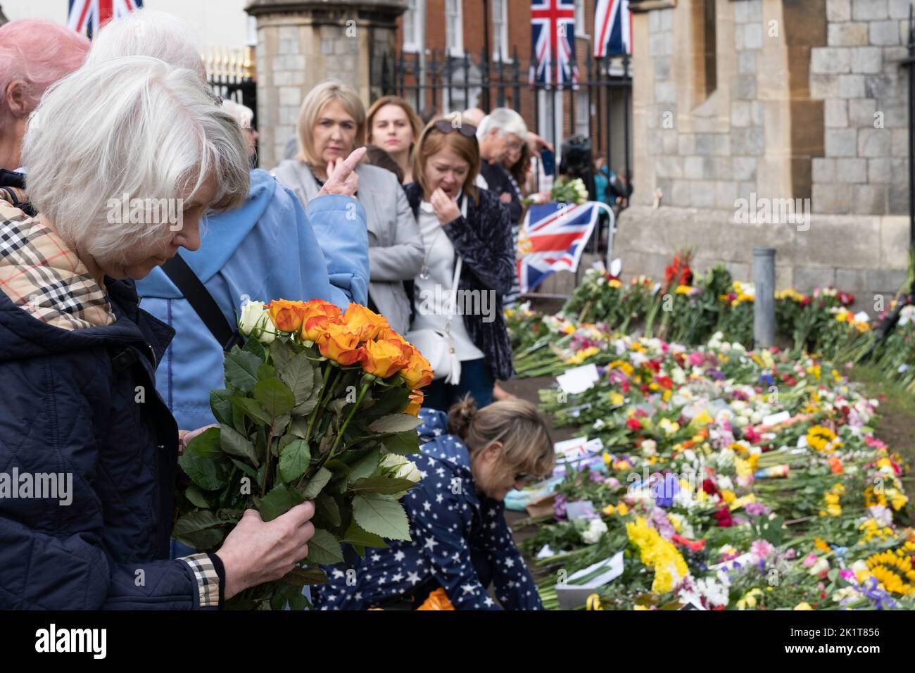 A woman is about to lay a bouquet of roses at the gates of Windsor