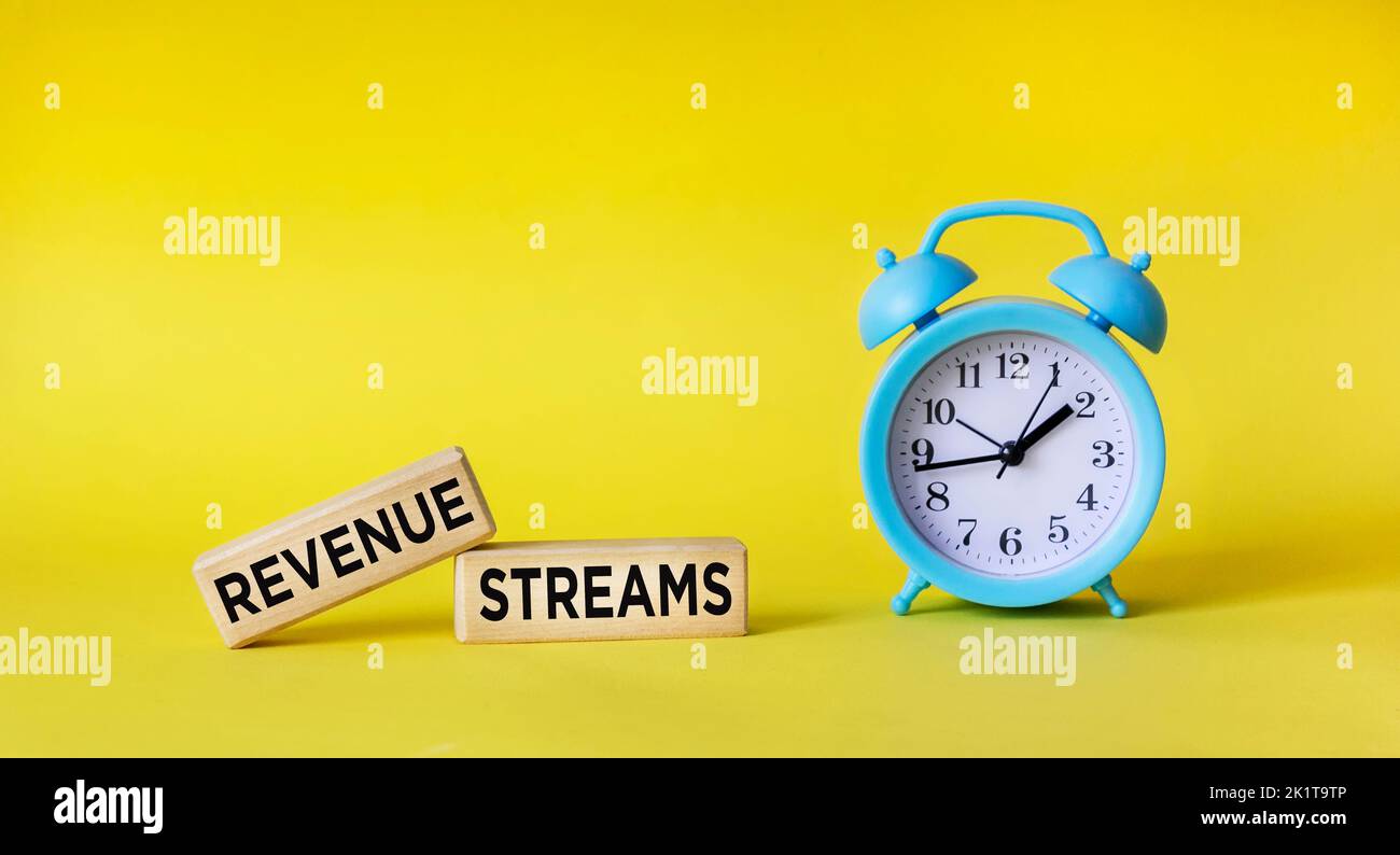 text REVENUE STREAMS on wooden blocks with clock, yellow background Stock Photo