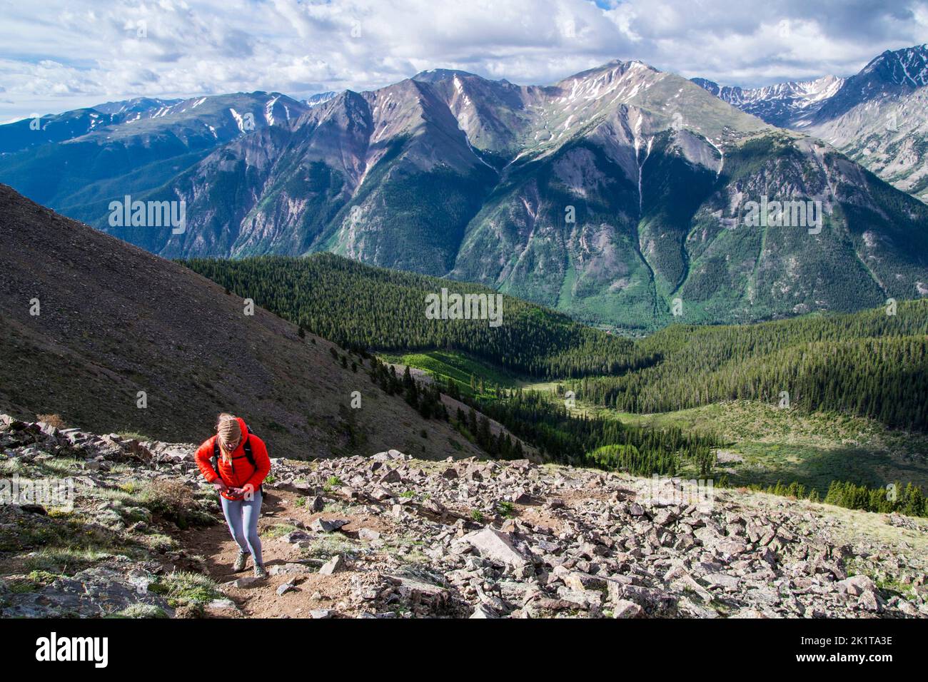 A woman climbs the steep walking trail on rocky ground with spectacular mountain views behind on Mt Elbert in Colorado USA Stock Photo