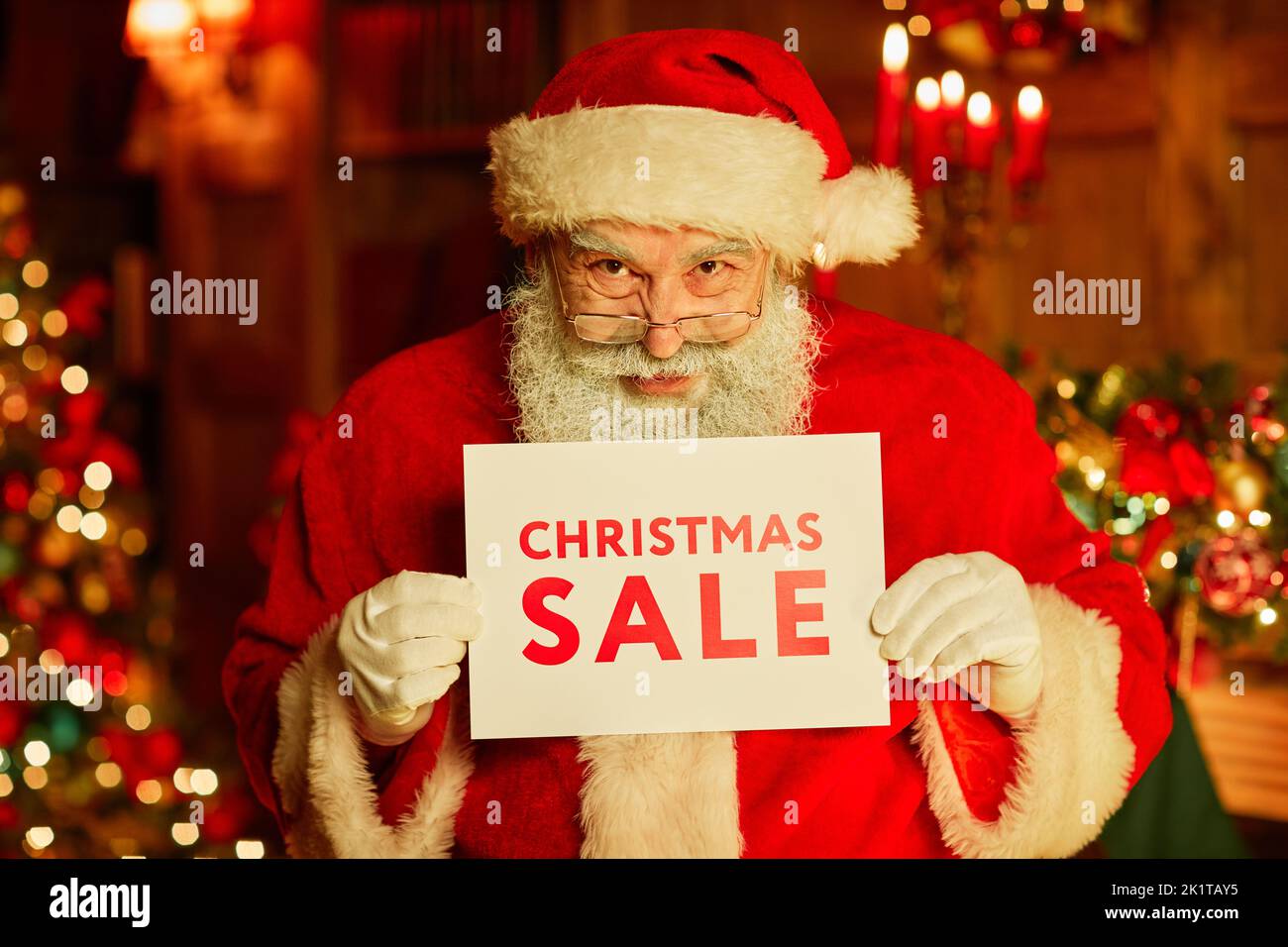 Waist up portrait of traditional Santa Claus holding Christmas SALE sign while standing in decorated room Stock Photo