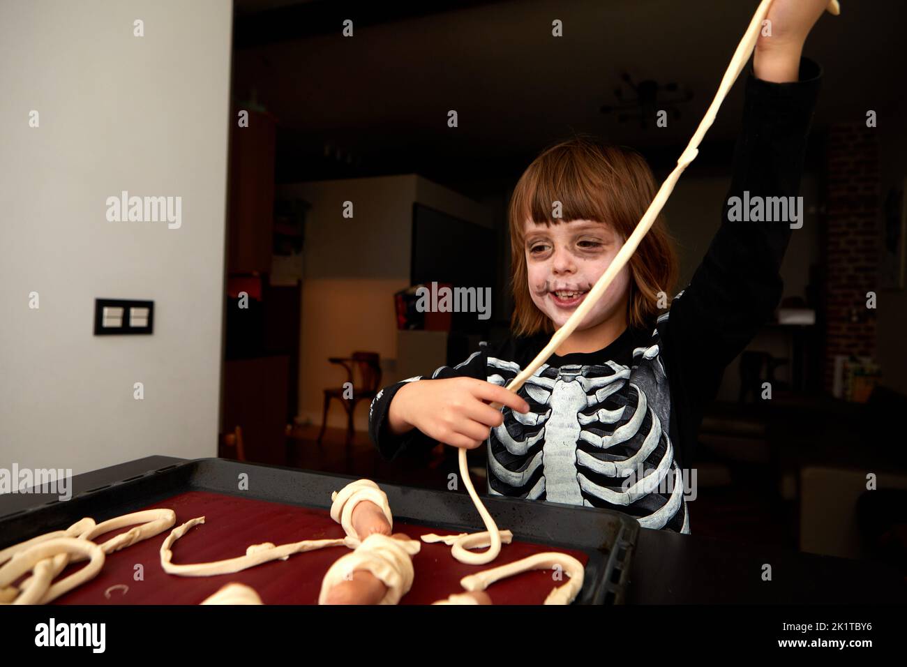 Cheerful kid in skeleton costume and makeup preparing pastries for baking on a baking sheet for the holiday halloween at home Stock Photo