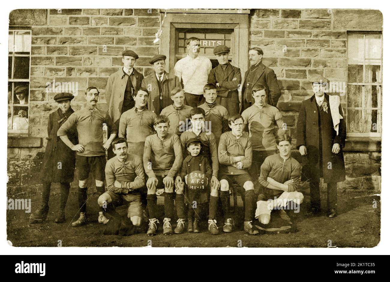 Original, clear early 1900's, postcard of football team and supporters who are wearing flat caps, posing for a photograph outside a pub. A young lad sits at the front holding a football marked with  'E.R. & S. AFC, 1911-1912',  U.K Stock Photo