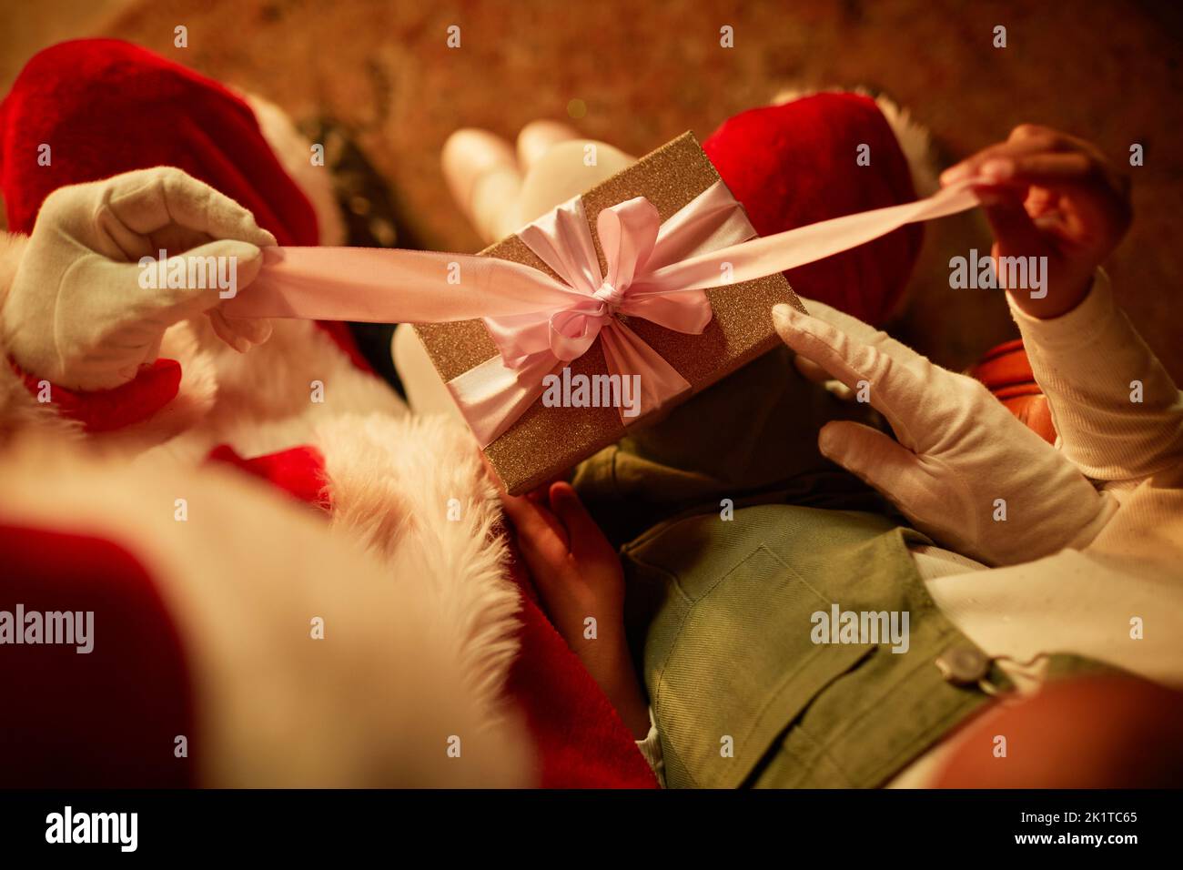 Top view closeup of little girl opening Christmas present while sitting in Santas lap, copy space Stock Photo