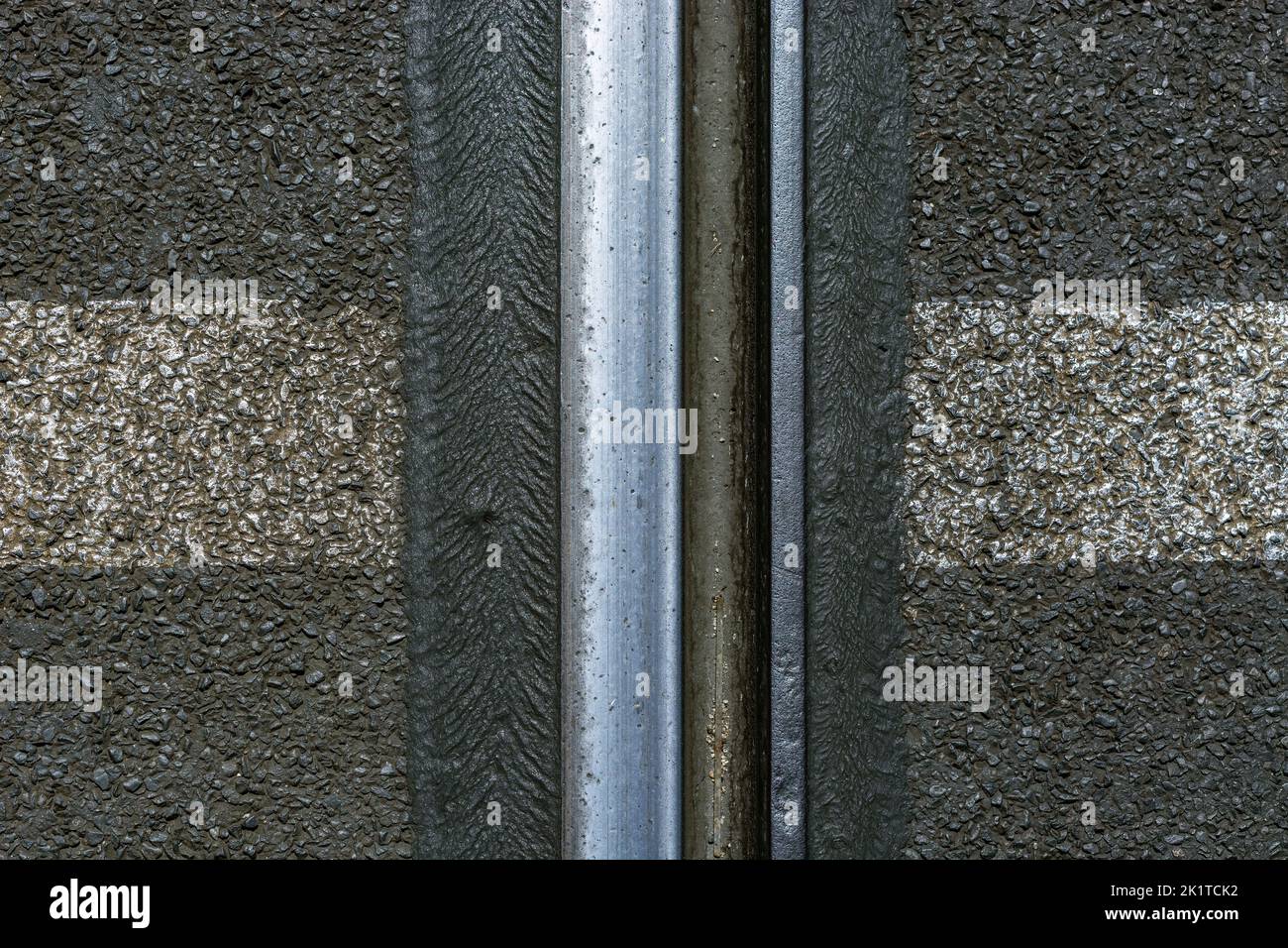 Fragment of a steel rail of a tram track on a background of gray asphalt. Stock Photo