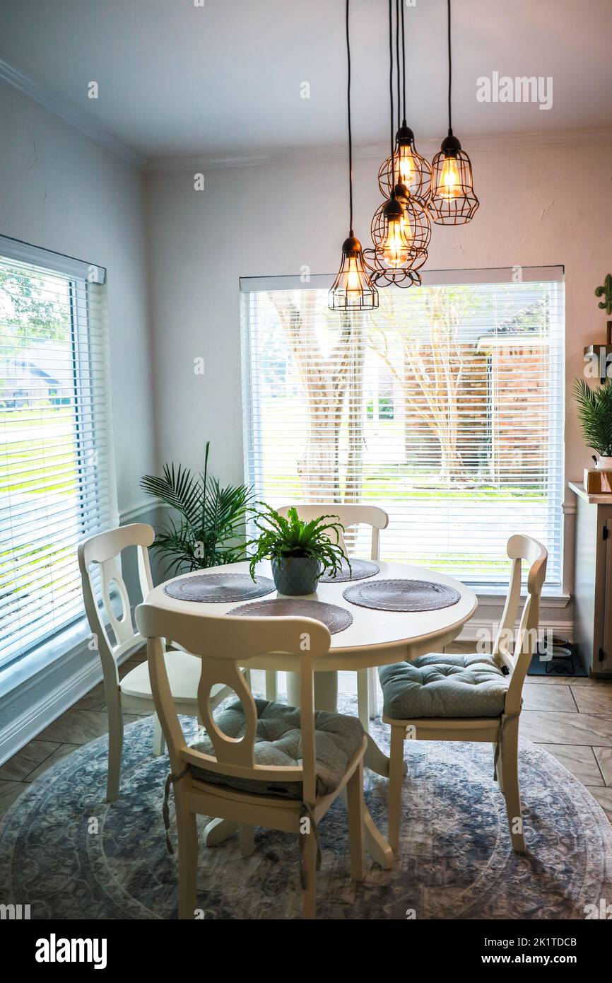 Small eat in kitchen with a tile floor and a white circle shaped table and four chairs with an industrial pendant lighting fixture, large windows, and Stock Photo