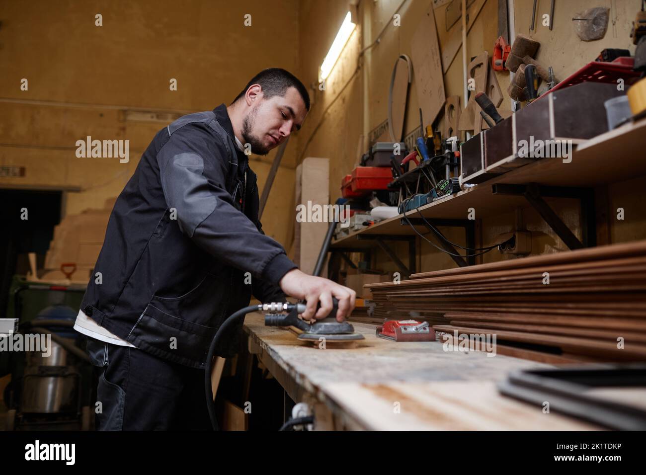 Side view portrait of male worker sanding wooden boards in workshop and using electric tools, copy space Stock Photo