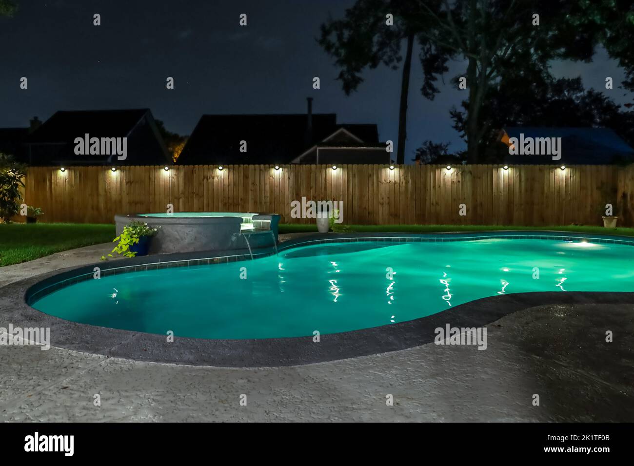 A backyard swimming pool and jacuzzi hot tob at night with solar lights around the fence for privacy and illumination. Stock Photo