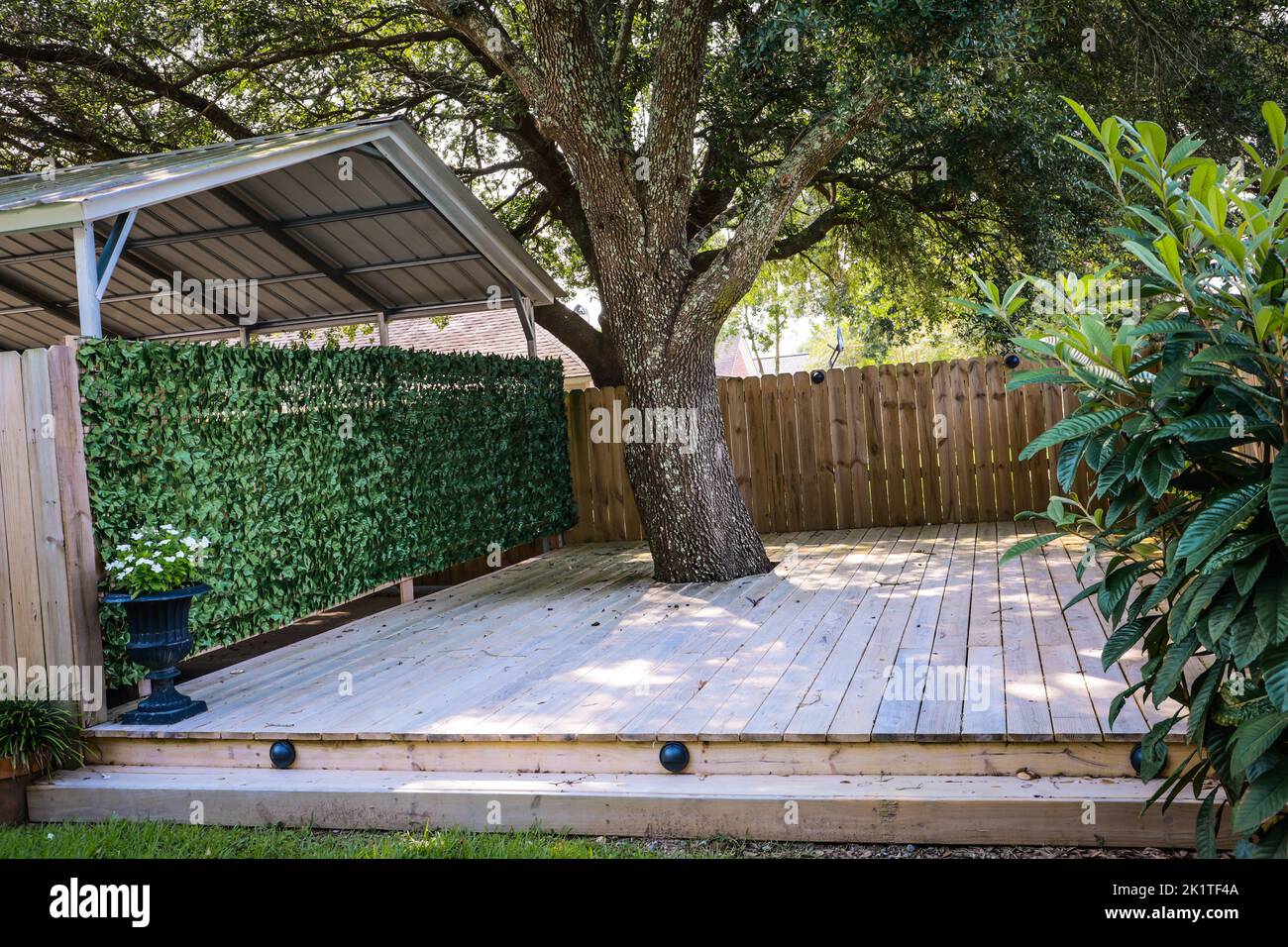 A small built out pressure treated wood deck space with a greenery covered wall to the garage Stock Photo