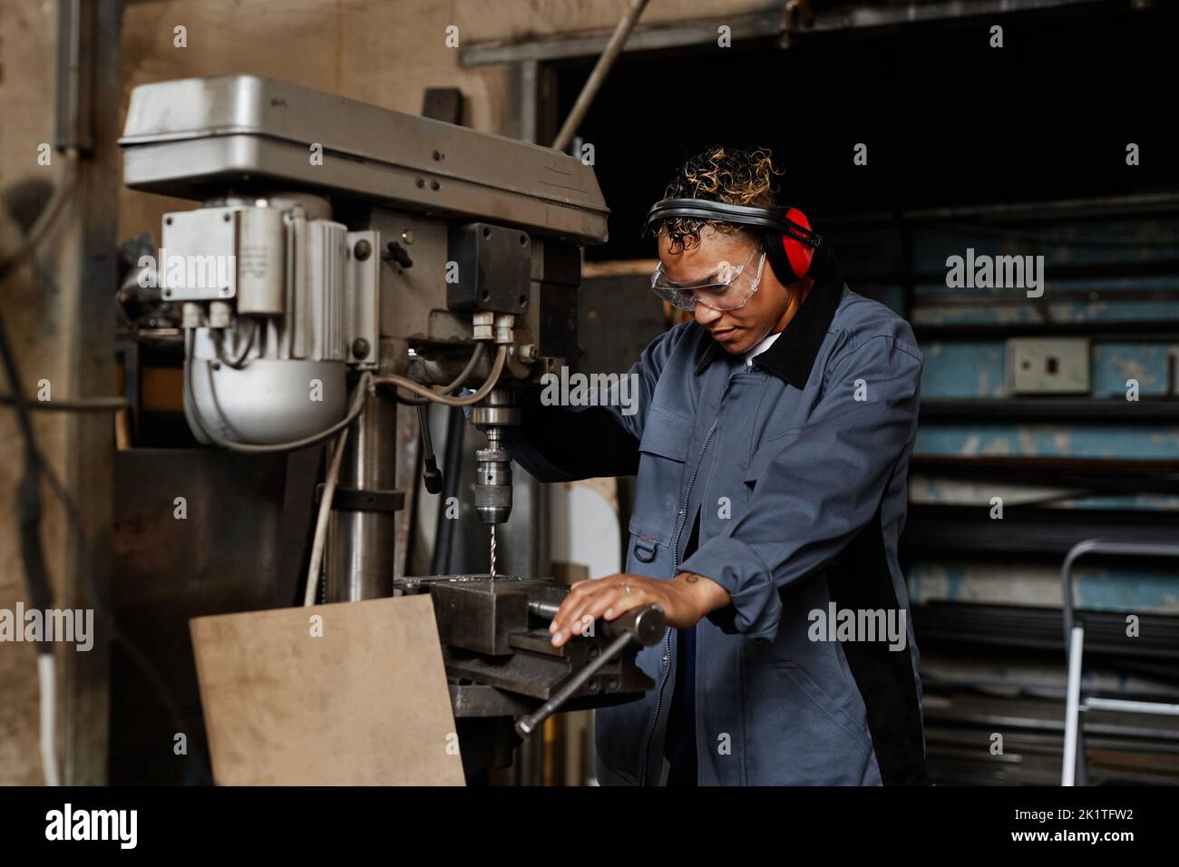 Waist up portrait of female worker operating machine unit and drilling ...