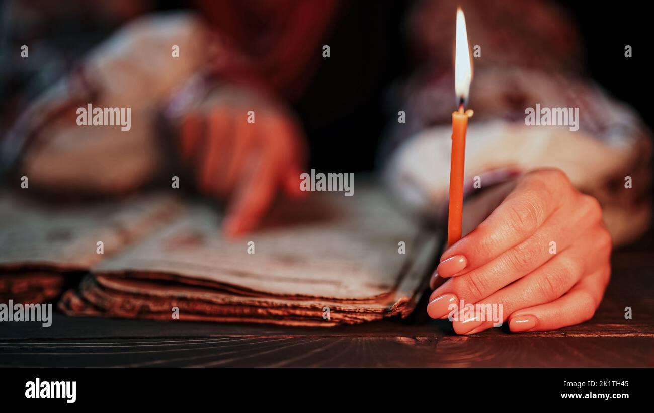 Ukrainian woman reading ancient book - Bible. Concentrated attentively follows finger on paper page under candle light. History of Kyiv Rus. Psalter Stock Photo