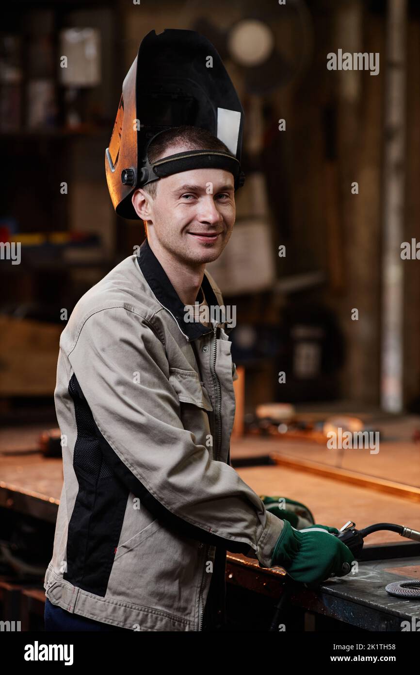 Vertical portrait of young male welder smiling at camera in industrial factory workshop Stock Photo