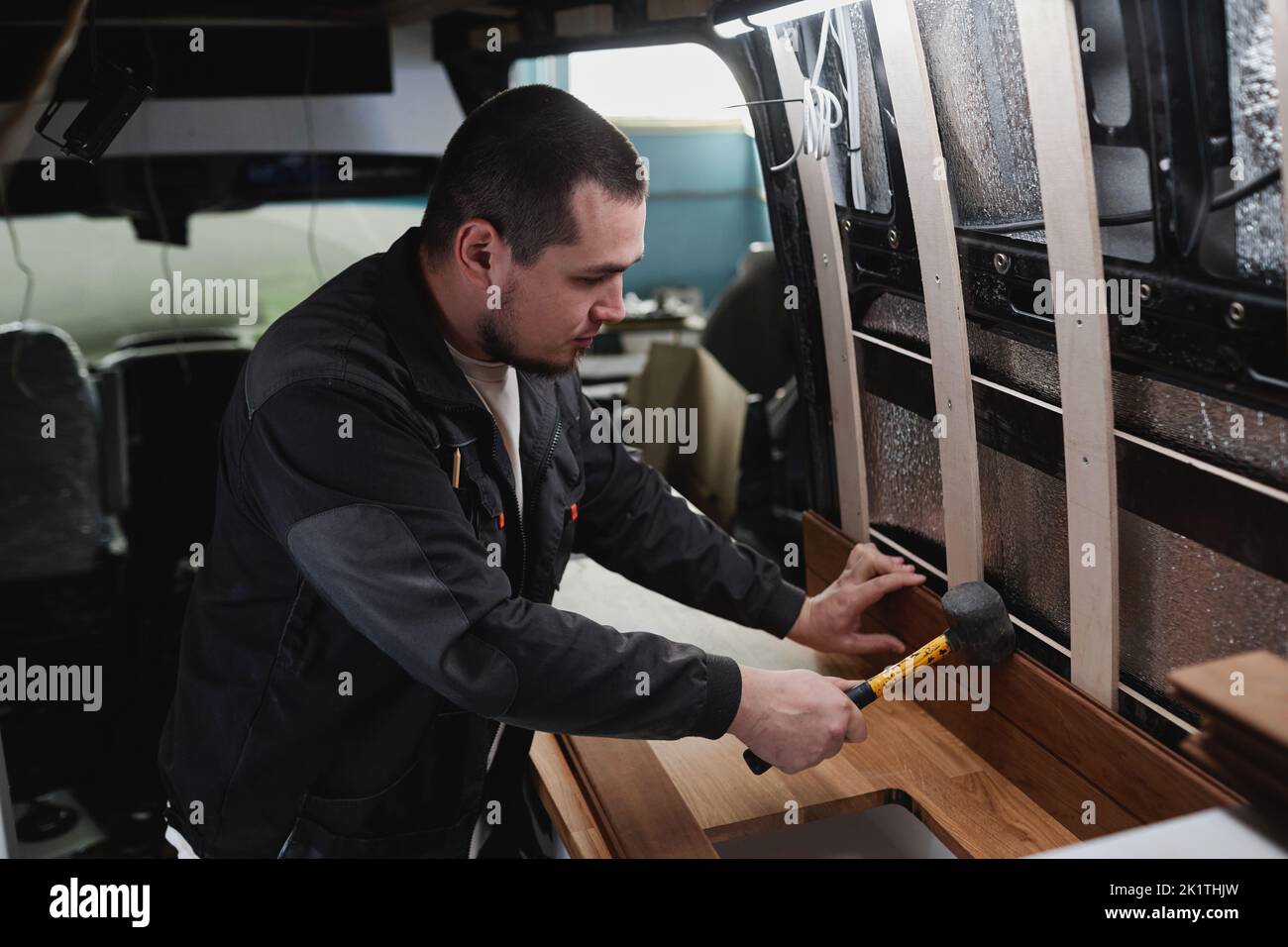 Side view portrait of young man building camper van and installing furniture in kitchen area Stock Photo