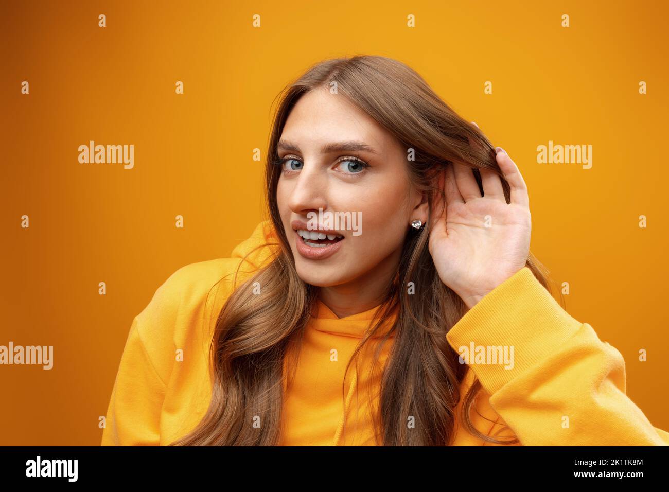 Young woman smiling with hand over ear listening and hearing on yellow background Stock Photo
