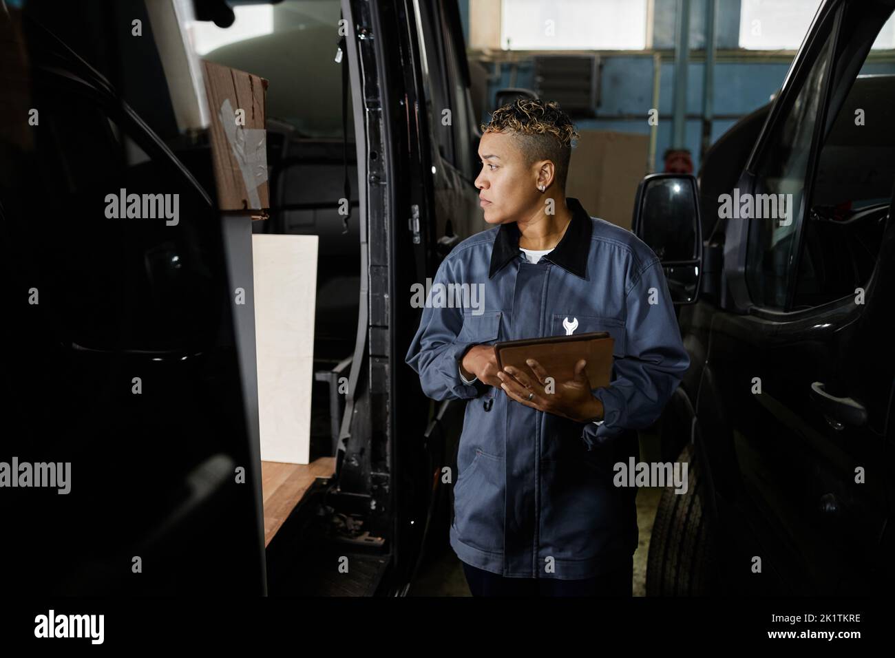 Side view portrait of female worker building vans and car factory and holding tablet with accent light Stock Photo