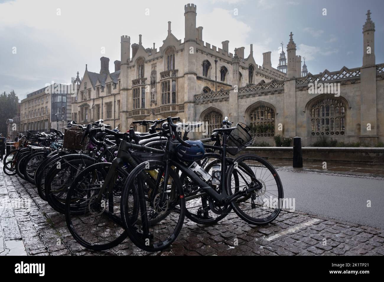 Bicycles parked on a wet street in front of the buildings of King's College. It's raining, white rain dashes and stripes on the bikes and background Stock Photo