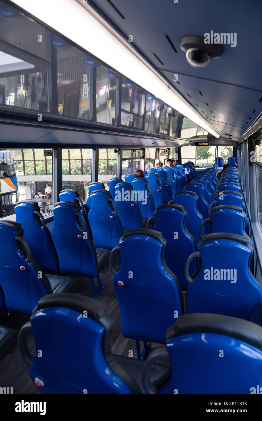 Interior of the upper deck in a modern double-decker bus with blue seats. There are a few passengers in the front. Focus in the front part of the bus Stock Photo